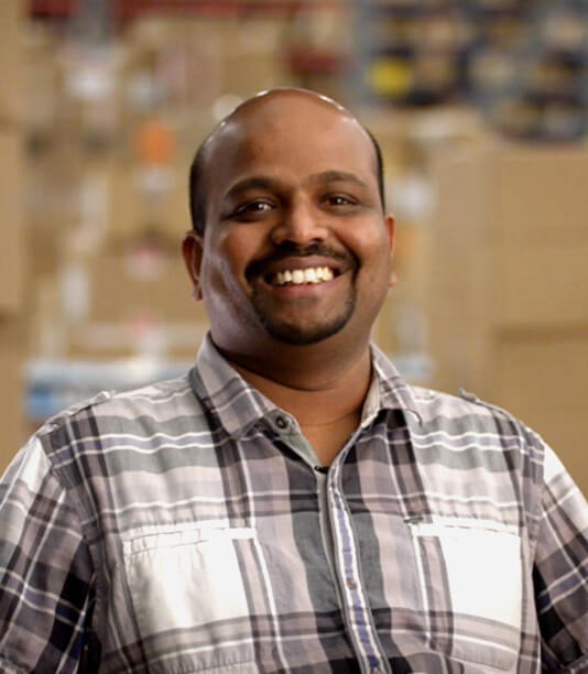 man with a grey and white plaid shirt smiles at the camera